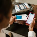 Pessoa realiza um pagamento digital pelo celular enquanto segura um cartão bancário.