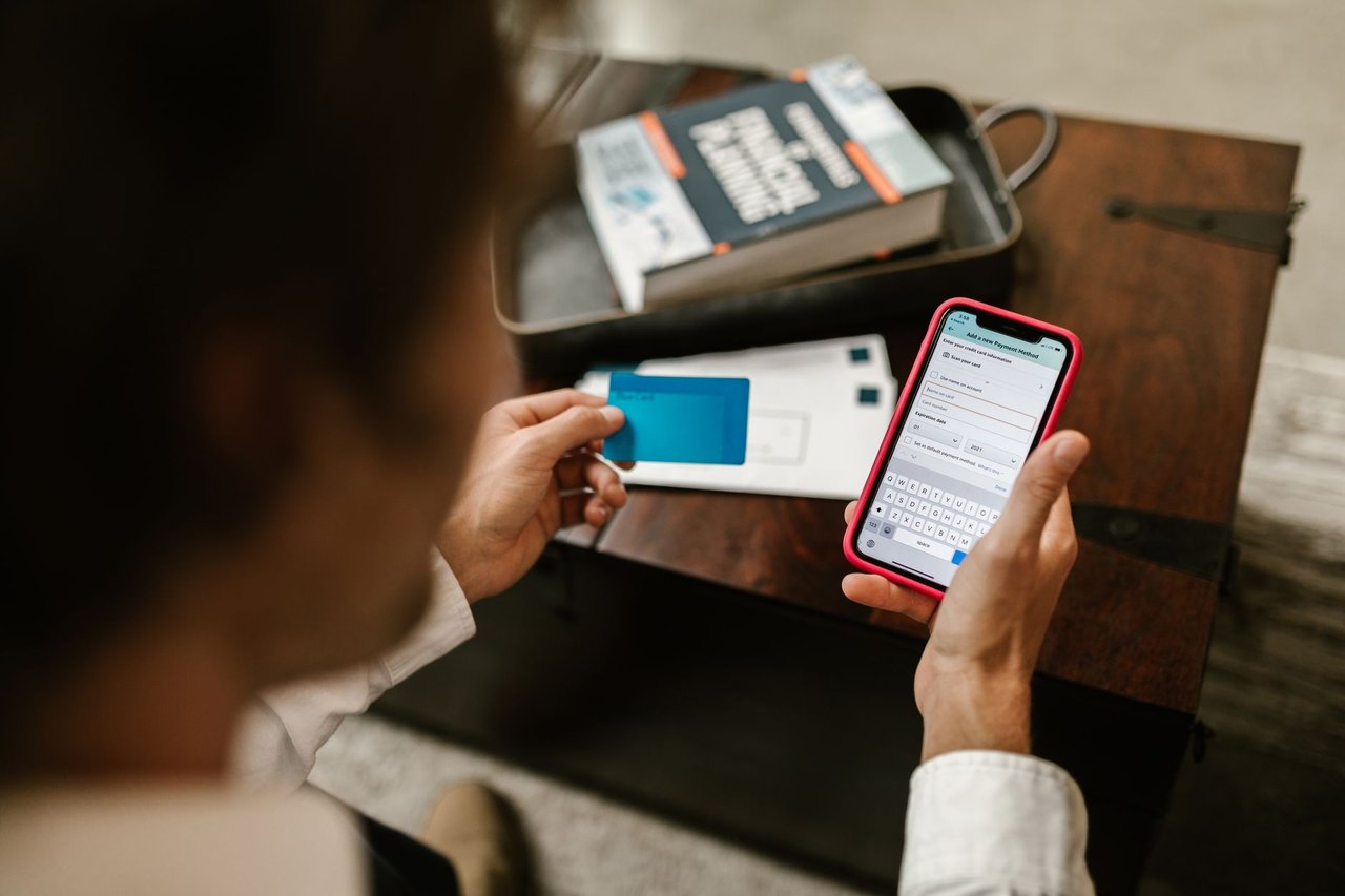 Pessoa realiza um pagamento digital pelo celular enquanto segura um cartão bancário.