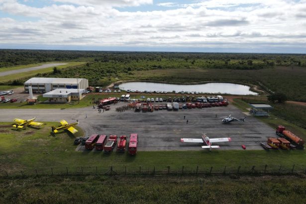 Vista aérea de uma base de combate a incêndios com caminhões, aeronaves e profissionais de emergência mobilizados.