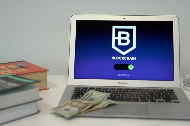Laptop exibe uma interface de conexão blockchain sobre uma mesa com livros e dólares americanos.