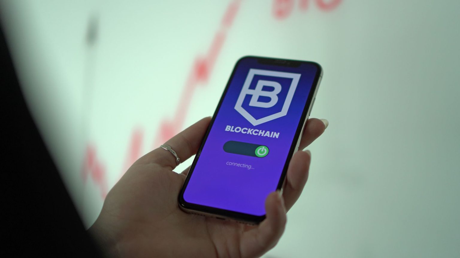 Mão segura um smartphone que exibe uma carteira digital de criptomoedas com interface de blockchain.