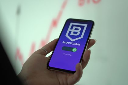 Mão segura um smartphone que exibe uma carteira digital de criptomoedas com interface de blockchain.
