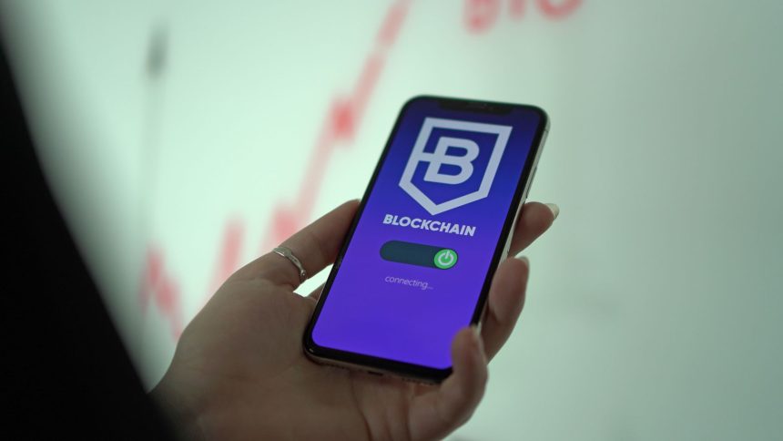 Mão segura um smartphone que exibe uma carteira digital de criptomoedas com interface de blockchain.